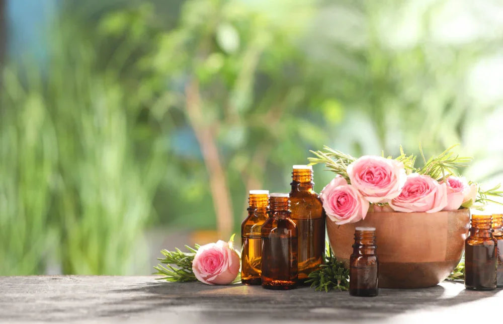 Bottles of essential oils for aromatherapy, roses, and rosemary on wooden table