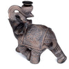 Angled view of a wood effect elephant incense burner, dark brown with intricate lighter brown traditional patterns. The elephant holds a small, black burner bowl on its raised trunk.