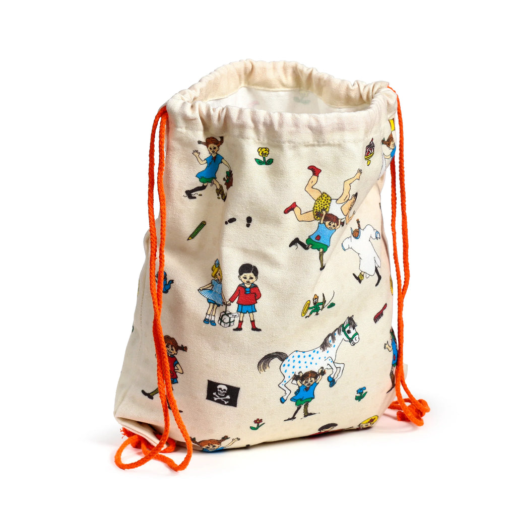 Angled view of a cream canvas drawstring bag, standing upright, with colourful Pippi Longstocking character illustrations and bright orange drawstrings.