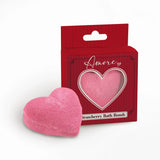Angled view of a pink heart bath bomb and its red gift box. The box features a heart-shaped window, 'Amore' text, and 'Strawberry Bath Bomb' text.