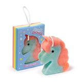 Angled view of a teal and coral unicorn soap sponge with a black eye and white hanging cord, positioned next to its light blue packaging box which features a rainbow stripe and a product window.