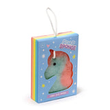 Angled view of a two-tone, unicorn-shaped soap sponge, visible through the window of its light blue, rainbow-striped box, with a white hanging loop.