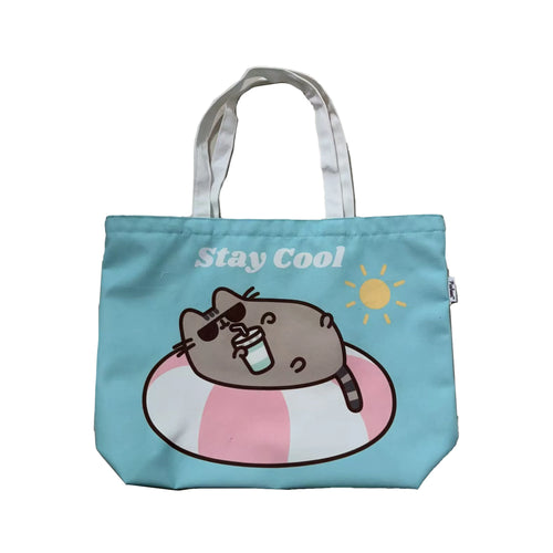 Front view of an aqua blue polyester beach bag with white fabric handles, depicting Pusheen the Cat wearing sunglasses, lounging in a pink and white striped inflatable ring with a drink, and the text 'Stay Cool'.