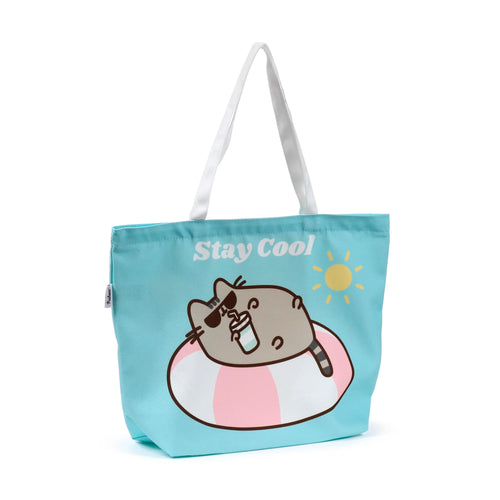 Front view of a turquoise beach bag featuring Pusheen the Cat wearing sunglasses in a pink and white inflatable ring, holding a drink with a straw. White text reads 'Stay Cool' next to a yellow sun.