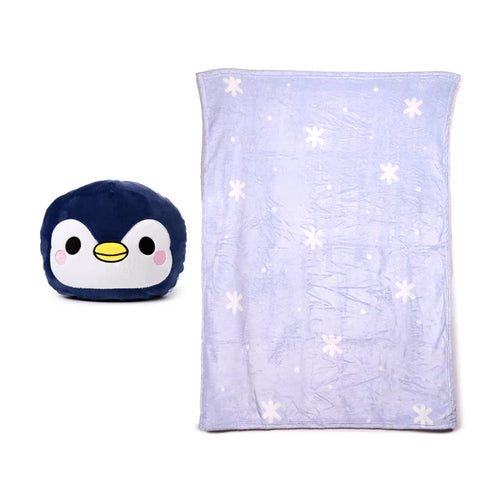 Front view of a dark blue penguin plush toy with white face and yellow beak, next to an unfolded light blue travel blanket featuring white snowflake patterns.