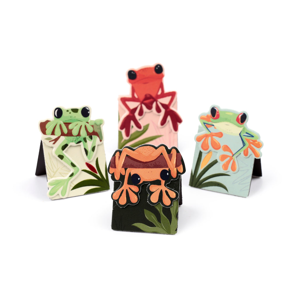 Angled view of a set of four colourful tropical frog magnetic bookmarks, each featuring a unique frog design peeking over green foliage, on a white background.
