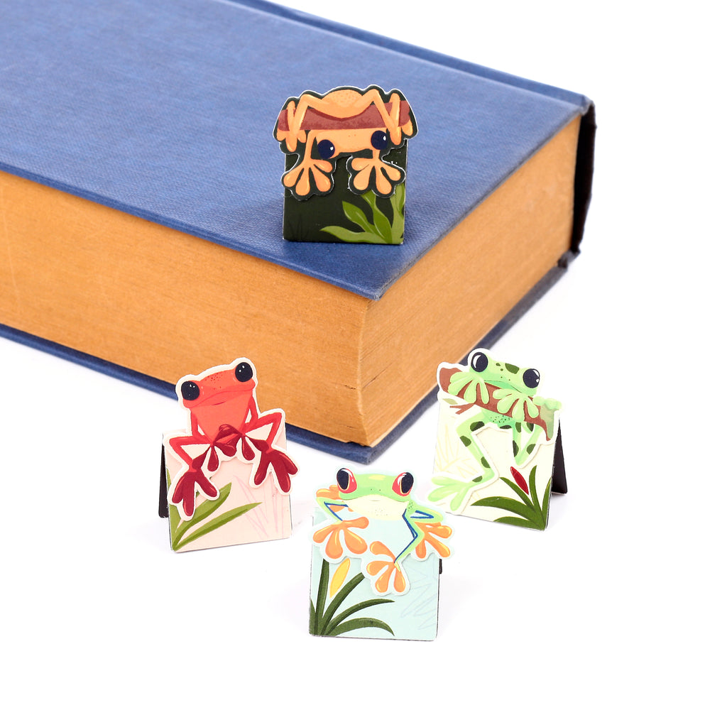Four colourful tropical frog magnetic bookmarks, including an orange frog on a blue book and three other frog designs standing on a white surface.