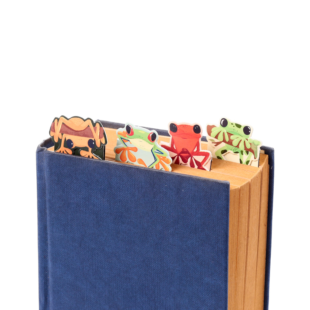 Close-up of four colourful tropical frog magnetic bookmarks, featuring green, red, and orange designs, peeking from the top of a blue book.