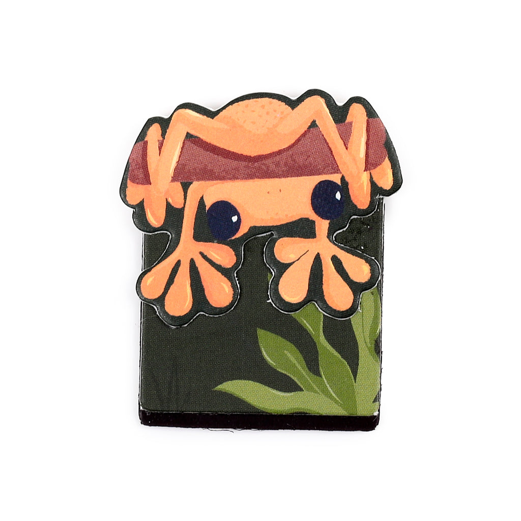 A single tropical frog magnetic bookmark, featuring an orange frog with prominent dark eyes and splayed legs, clinging to a dark green base with subtle leaf patterns.