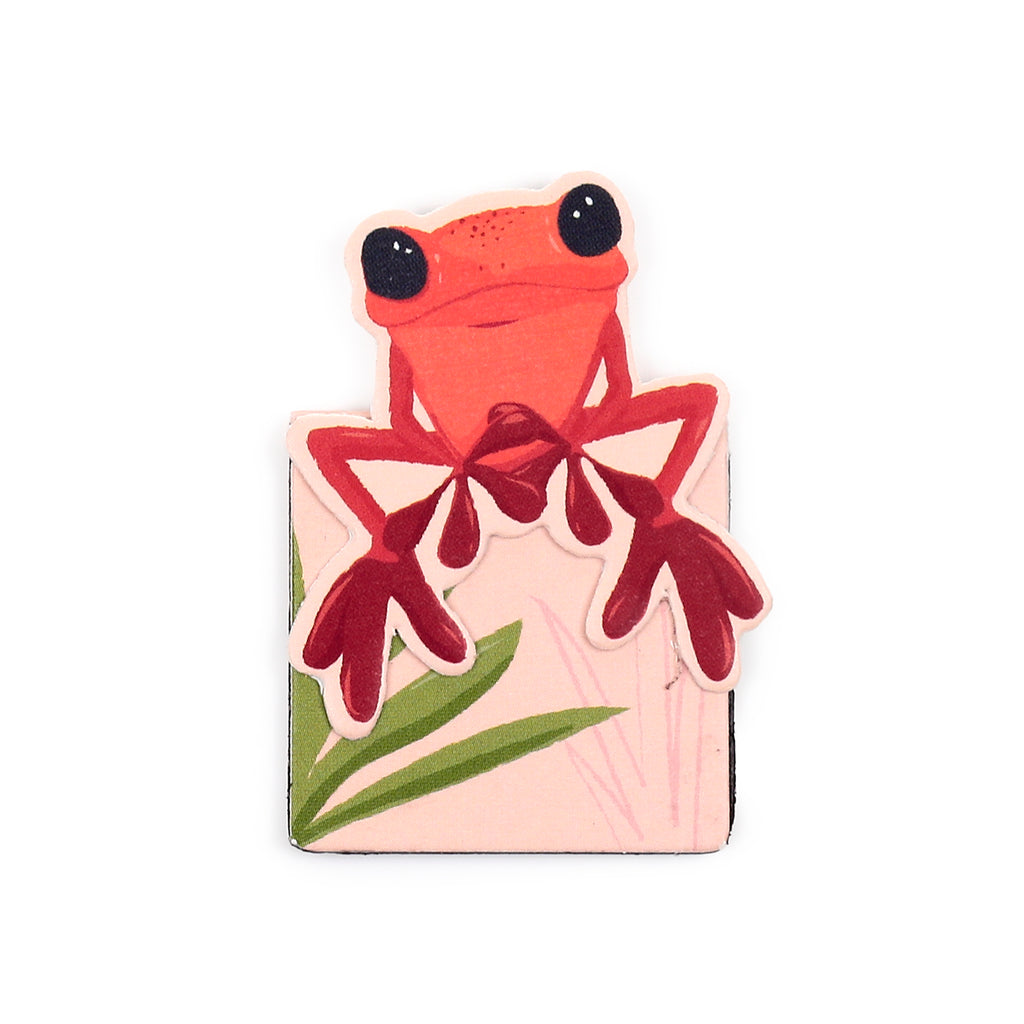 Front view of a tropical red frog magnetic bookmark, featuring a stylised red frog with black eyes and green leaves on a light peach background.