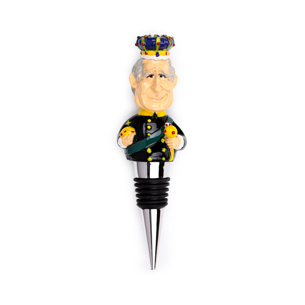 Front view of a King Charles III novelty bottle stopper, depicting a caricature of the King wearing a colourful crown, a black uniform with a green sash, and holding an orb and sceptre, with a silver-coloured metal stopper and black rubber rings.