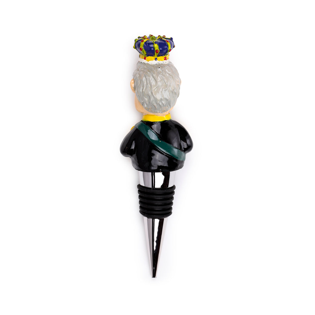 Back view of a novelty King Charles III bottle stopper, depicting the figurine wearing a black uniform with a green sash and a blue jewelled crown, with grey hair visible.