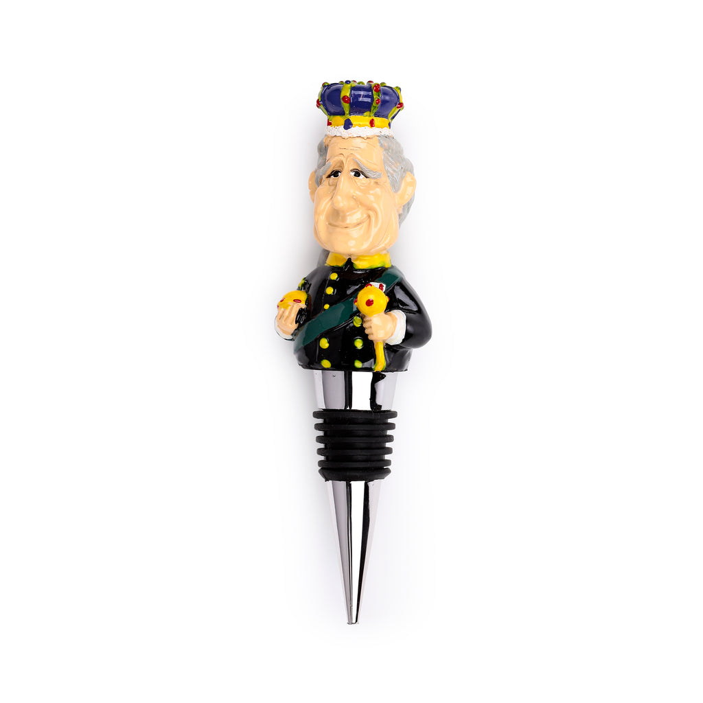 Front view of a novelty bottle stopper, depicting a caricature of King Charles III. He wears a blue, yellow, and red crown, a black ceremonial uniform with a green sash, and holds an orb and sceptre. The stopper features a silver-coloured base with black rubber rings.