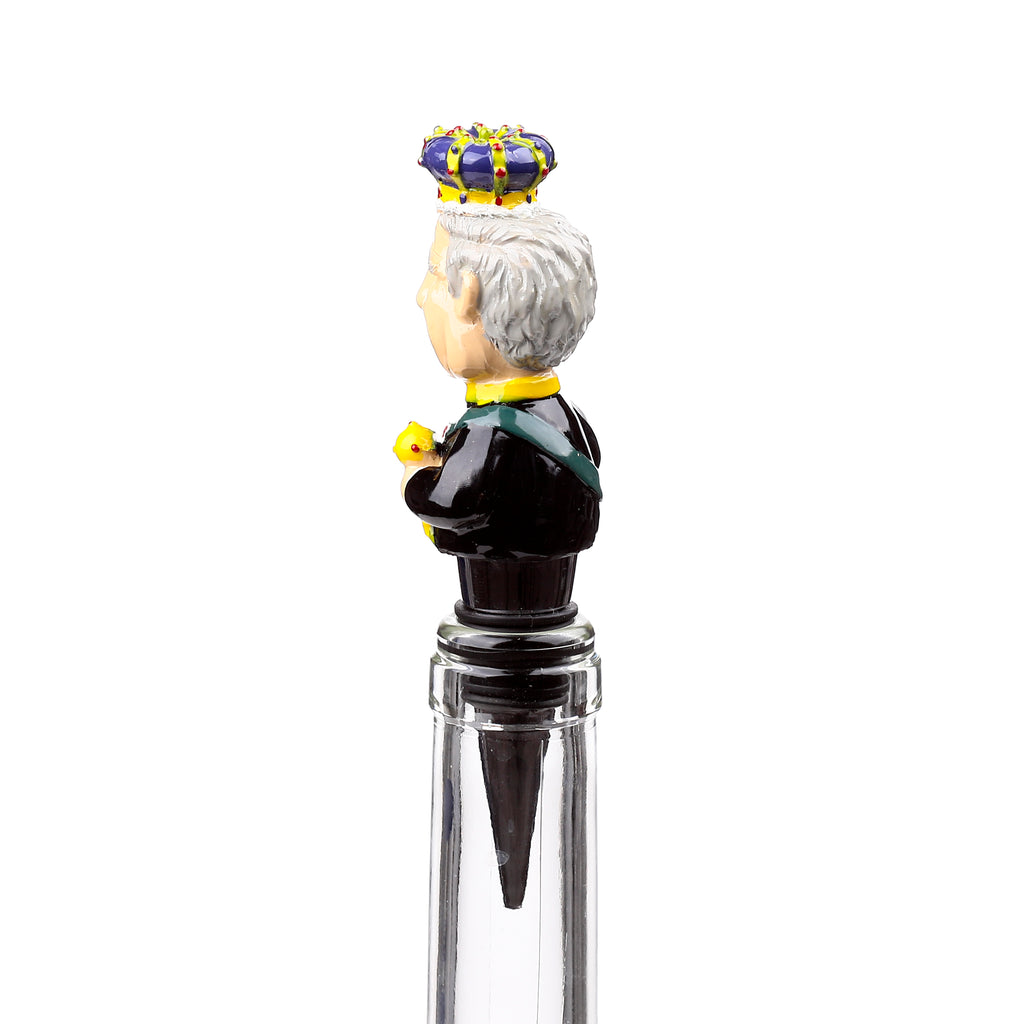 Side view of a novelty King Charles III bottle stopper, depicting the monarch with grey hair, a purple and gold crown, a black uniform with a green sash, holding a small yellow object, fitted into a clear glass bottle.