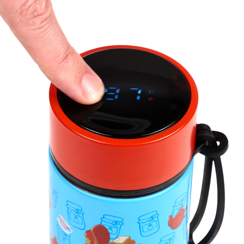 Close-up of a finger pressing the digital thermometer display on the red and black lid of a light blue insulated drinks bottle, showing '37 °C'. The bottle's body features a pattern of jam jars and bread, with a black carry strap visible.