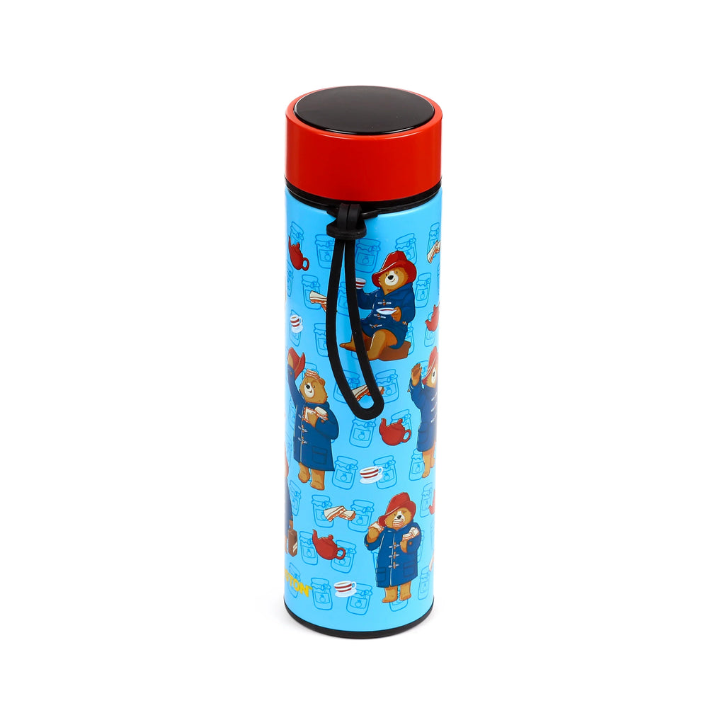 Angled view of a light blue reusable insulated drinks bottle, decorated with a repeating pattern of Paddington Bear in a blue duffle coat and red hat, with a red cap and black carrying loop.
