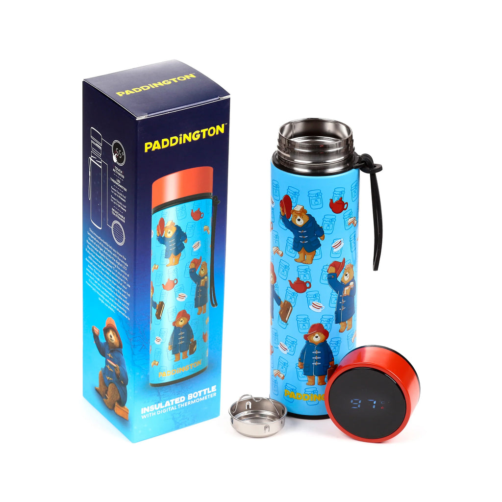 Arranged product shot showing a light blue insulated drinks bottle featuring Paddington Bear, jam jars, and teapots, alongside its detached red digital thermometer lid displaying 97°C, a metal tea strainer, and its dark blue packaging box on a white background.