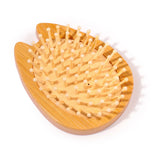 Angled view of a natural bamboo, cat-shaped hair brush featuring light-coloured bamboo pins set into a pale beige, textured base.