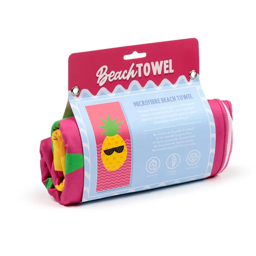 Angled view of a rolled, colourful microfibre beach towel in its bright pink packaging. The packaging prominently displays the 'Good Vibes Pineapple' cartoon graphic, featuring a pineapple wearing sunglasses.