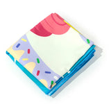 Angled view of a folded microfibre beach towel, featuring a colourful unicorn-themed design in pink, cream, and purple with sprinkles, revealing a bright blue underside.