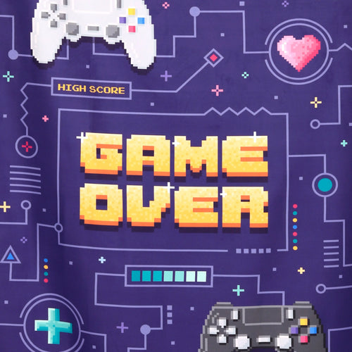 Close-up of a microfibre beach towel showing a pixelated 'GAME OVER' design in golden letters, surrounded by white and black game controllers, a pink heart, 'HIGH SCORE' text, and other gaming icons on a deep purple background.