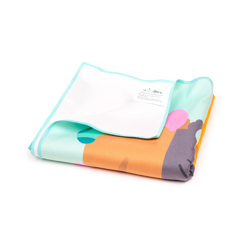 Angled view of a folded microfibre beach towel with abstract orange, grey, pink, and light blue patterns, showing the plain white reverse and a light blue stitched edge.