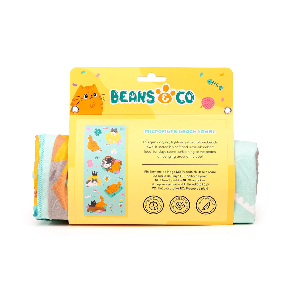 Front view of a microfibre beach towel in its yellow retail packaging, featuring an orange cartoon cat logo and illustrations of various cats. The packaging highlights the towel's quick-drying and ultra-absorbent properties, with the folded towel's colourful patterned edge visible on either side.