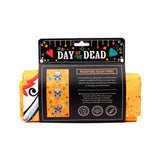 Packaged Day of the Dead microfibre beach towel, displaying its black retail header with colourful decorative elements and text, alongside the towel's orange sugar skull pattern.