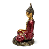 Side view of a red and gold Thai Buddha figurine seated in contemplation, with intricate gold detailing on robes and an ornate base.