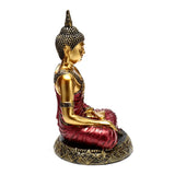 Right profile view of a golden Thai Buddha figurine with red robes, seated in meditation, on an ornate, patterned base.