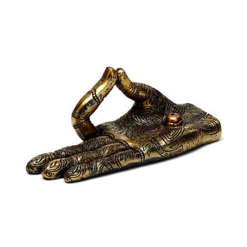 Angled view of an antiqued gold incense holder shaped like a Buddha hand, featuring intricate henna-style patterns and a small incense stick hole in the palm.