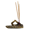 Angled view of a metallic gold ashcatcher incense holder, shaped like a Buddha hand with intricate henna-like patterns, holding three brown incense sticks with purple bases.