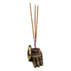 Angled view of a gold-coloured, hand-shaped incense holder, intricately decorated with henna-style patterns across its palm and fingers, featuring three brown incense sticks, against a white background.
