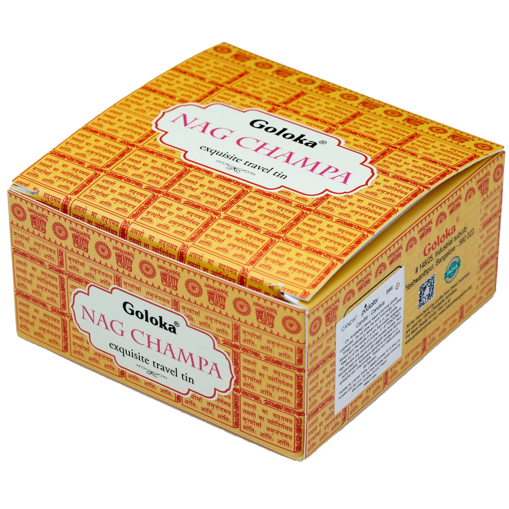Angled view of the rectangular Goloka Nag Champa wax candle tin packaging. The box features a yellow background with repeating red Sanskrit script and decorative patterns, displaying the text 'exquisite travel tin' on the front.