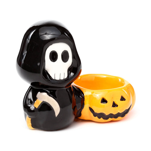 Angled view of a glossy black ceramic 'Skull Boy' tea light holder, featuring a white skull face, a beige scythe, and an integrated orange jack-o'-lantern.