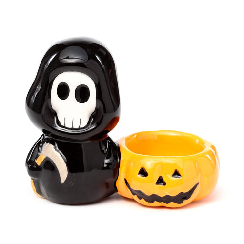 Front view of a glossy black ceramic skull figure with a white face and grey scythe, next to an orange jack-o'-lantern pumpkin tea light holder.