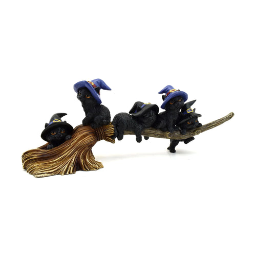Angled view of a Witches Cat ornamental figurine featuring five black cats with orange eyes wearing witches' hats with gold buckles, playfully perched and hanging on a textured brown broomstick.
