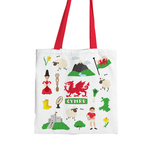 Front view of a white shopping tote bag with red handles, featuring a vibrant illustration of Welsh cultural symbols including the red dragon, Welsh flag, sheep, daffodils, leeks, a Welsh lady, rugby ball, love spoon, castle, and map of Wales, with 'CYMRU' text.