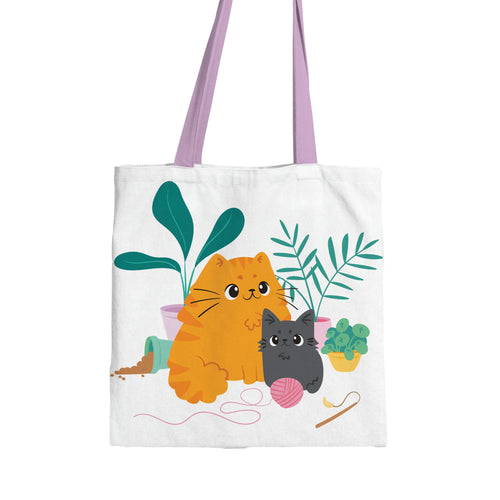 Front view of a white tote shopping bag with a colourful illustration of an orange tabby cat and a grey cat amongst green potted plants and a pink ball of yarn, with pale lilac handles.