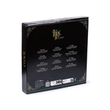 Angled view of black wall clock packaging, showing the Lisa Parker logo on the ribbed top, gold 'CLOCK' text on the side, and multi-language details regarding battery requirements, alongside gold and green Celtic knot patterns.