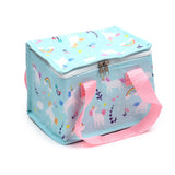 Angled view of a light blue cool bag with a colourful unicorn, rainbow, and star pattern, featuring pink fabric carry handles and a white zip closure.