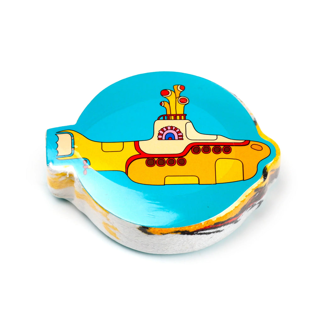 Angled view of a compact, compressed travel towel, featuring The Beatles Yellow Submarine design in yellow, red, and black against a turquoise blue background.