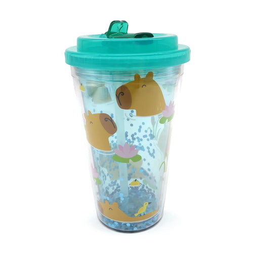Angled view of a clear double-walled cup featuring brown capybara illustrations, pink water lilies, small yellow birds, and blue hexagonal glitter. The cup has a teal lid with a flip-top sipper and a clear straw inside.