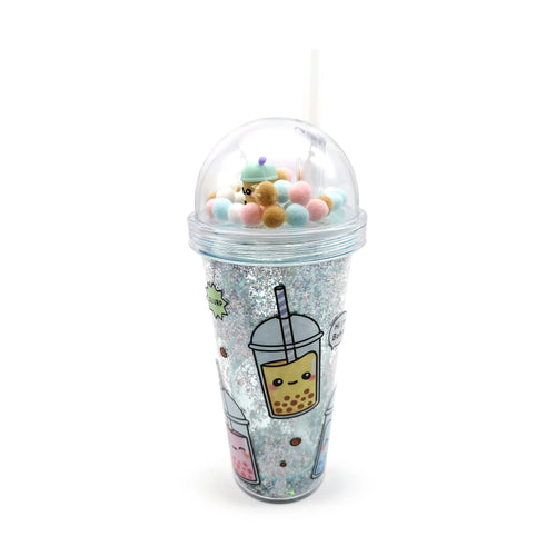 Angled view of a double-walled clear cup, filled with silver glitter and decorated with cartoon bubble tea images. It has a clear dome lid containing colourful pom-poms and a miniature bubble tea charm, with a white straw.