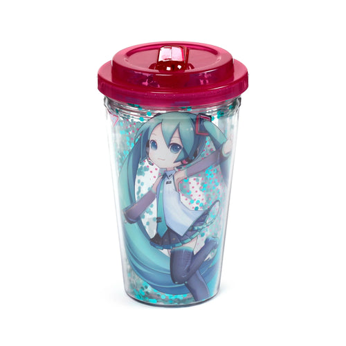 Angled view of a clear double-walled cup with a bright pink lid and clear flip-top closure. The cup displays a Hatsune Miku character graphic and contains turquoise and pink glitter between its walls.