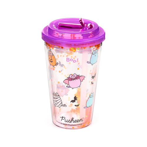 Angled view of a clear, double-walled cup with a purple lid and matching straw, containing orange and yellow hexagonal glitter. The cup is decorated with Halloween-themed Pusheen the Cat illustrations, including a pumpkin, vampire, and mummy, alongside black bat silhouettes and purple 'Boo!' text.