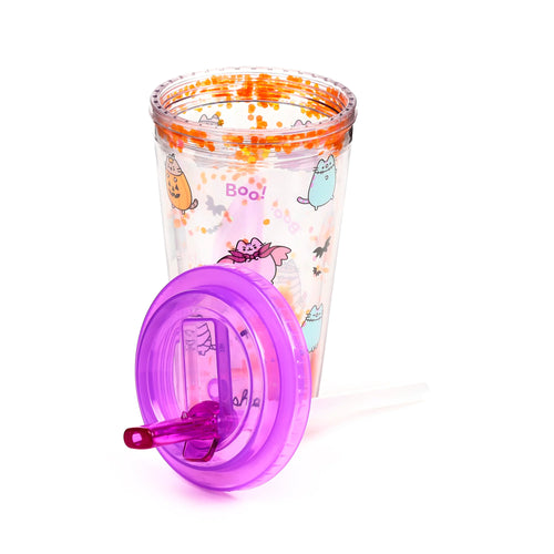 Angled view of a clear double-walled cup featuring Halloween Pusheen the Cat designs and orange glitter, with its purple lid and clear straw lying detached beside it.