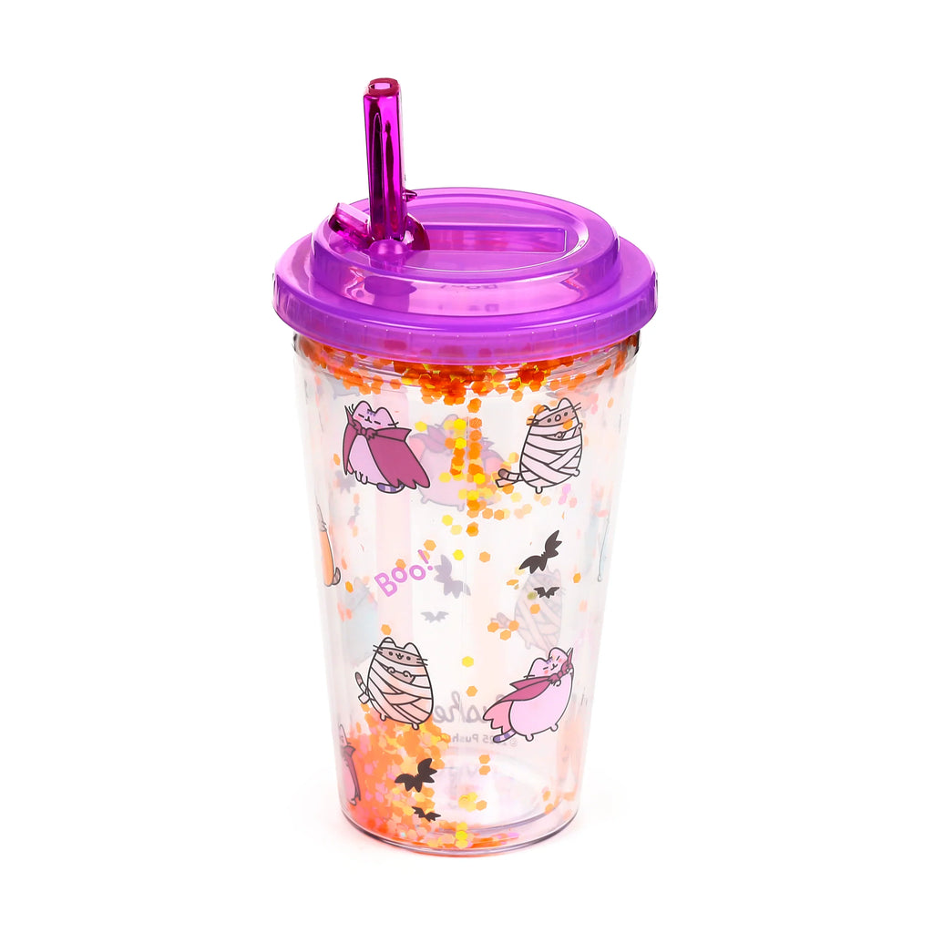 Angled view of a clear double-walled cup with a purple lid and straw, featuring Halloween Pusheen the Cat mummy and vampire designs, 'Boo!' text, bats, and internal floating orange glitter.