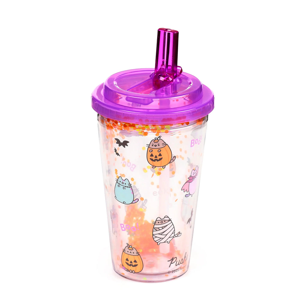 Angled view of a clear shatterproof double-walled cup with a purple lid and matching straw. The cup features Halloween Pusheen the Cat designs, including Pusheen as a pumpkin, mummy, and ghost, with bats and 'Boo!' text, and contains orange and yellow glitter.