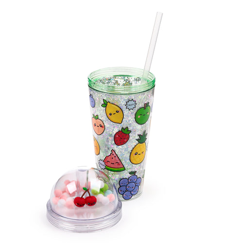 Angled view of a double-walled cup with a clear straw and a detached clear lid. The cup features a sparkly inner wall with holographic glitter and stars, and an outer wall decorated with colourful cartoon fruit characters. The lid contains red cherry charms and assorted pink, white, green, and blue pom-poms.